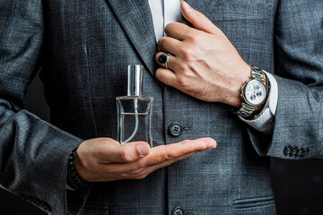 Male holding up bottle perfume. Hand in with wrist watch in a business suit. Perfume or cologne...