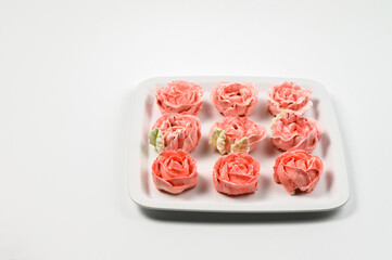 Pink marshmallows laid out in rows on a square white plate. white background.