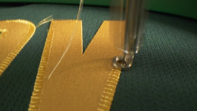 Machine embroiders golden letter on green fabric of uniform
