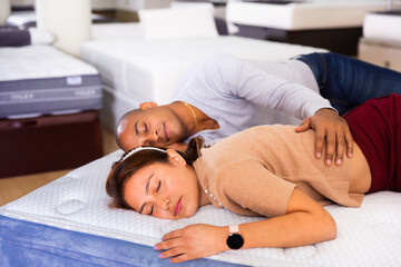 Young glad beautiful latin american couple sleeping on display sample bed with orthopedic mattress...