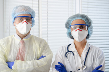 Fototapeta na wymiar Male and female health care workers in masks glasses caps and gloves standing with arms crossed