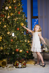 Cute little girl decorating christmas tree on New Year's eve. Vertical photo of female child in festive room with xmas fir tree at night.