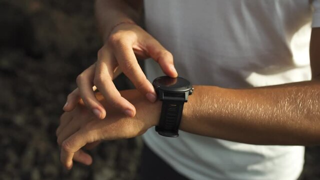 Young athletic man using fitness tracker or smart watch before run training outdoors. Close-up, slow-mo with dark background.
