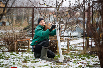 Caucasian woman gardener warming a bush for the winter, seasonal work in the garden close-up.