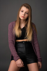 beautiful girl teenager in leather shorts and a lilac cardigan posing in the studio on a gray background