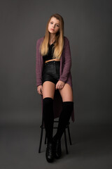 Obraz na płótnie Canvas beautiful girl teenager in leather shorts and a lilac cardigan posing in the studio on a gray background
