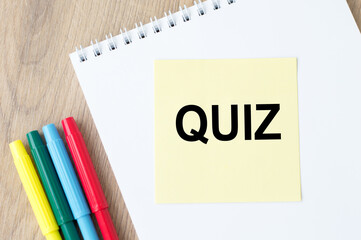 the inscription on the yellow sheet for notes text QUIZ which is attached to the notebook on the table.