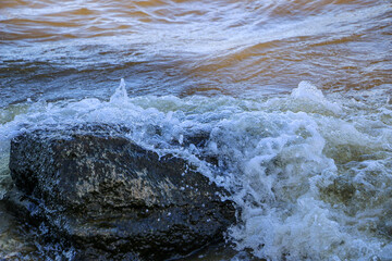 waves run onto the shore and crash against the rocks, creating many splashes and splashes near the shore. river surf in stormy weather near a stone pebble coast with foamy splashing waves.