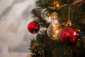 Glass glowing light bulb on a branch of a Christmas tree among other Christmas decorations and with garland lights