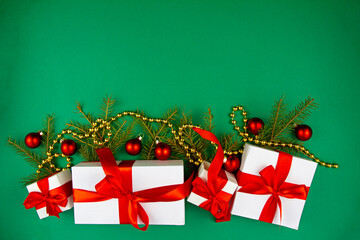 Craft gift boxes with a red satin bow and spruce branches decorated with Christmas balls on a green background. The festive concept. Copy space