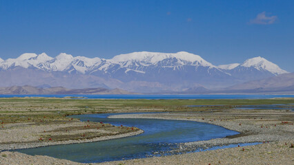 Snow-capped mountains with river foreground around Karakul lake, Murghab district, Gorno-Badakshan, in the Pamir region of Tajikistan