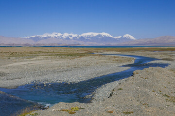 View from the shores of Karakul lake after sunrise, with Zulumart snow-capped mountain range and river in foreground, Murghab district, Gorno-Badakshan, in the Pamir region of Tajikistan