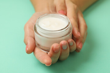 Cute female hands hold jar of cosmetic cream on mint background