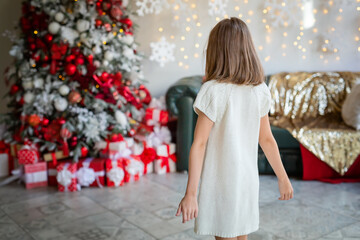 X-mas, winter, happiness concept - happy girl with many gift boxes. A five-year-old girl near a Christmas tree. A beautiful baby girl in a white dress is ready to celebrate on New year's eve