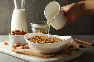 Female hand pour milk in bowl with granola