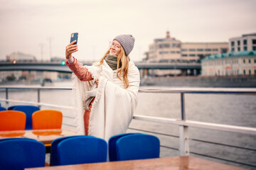Red-haired woman in glasses traveler in a hat and jacket making a selfie in Moscow on a pleasure boat on the river in the center