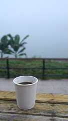 Hot coffee in white paper cup on rustic timber table