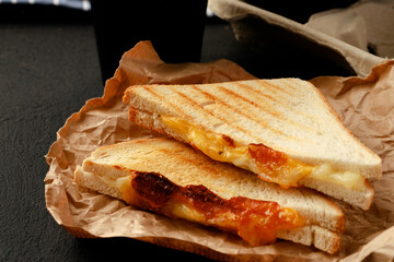 Toasted sandwich in craft paper with cup of coffee on table