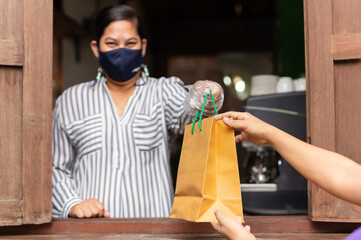 Social distance conceptual waitress giving takeaway bag to customer at cafe.