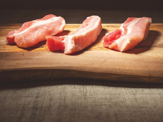 Three fresh uncooked pork belly portions on a wooden cutting board. Meat industry product
