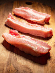 Three fresh uncooked pork belly portions on a wooden cutting board. Meat industry product
