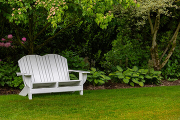 Obraz premium An Isolated View of English Style Garden Path with Manicured Lawn, Hostas, Trees, and White Adirondack Garden Bench - Daytime, No Sky