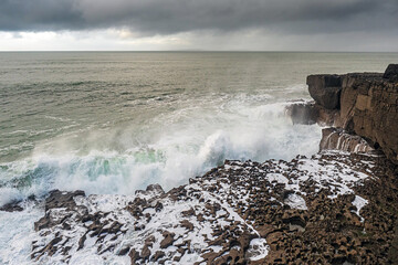 Powerful waves hit the rough stone coast line creating huge splashes of water. Low dark storm clouds, West of Ireland. Nobody.