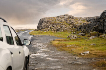 Small asphalt road on West coast of Ireland, Stone terrain in focus, white car parked off road out...
