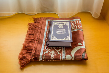 A holly Quran book on a traditional Arabic carpet at the window under sunlight at the room of hotel