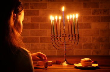 Low key image of jewish holiday Hanukkah background with girl looking at menorah (traditional candelabra) and burning candles