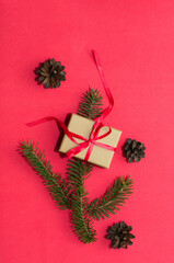 Natural spruce tree branch with a fir cone and Christmas decorations on a red background. Merry christmas and New Year. A minimalist composition, celebration and giving gifts. Copy space, flat lay.