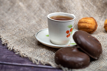 A small mug of tea, chocolate cake and homemade cookies on a background of coarse homespun fabric. Close-up, selective focus.