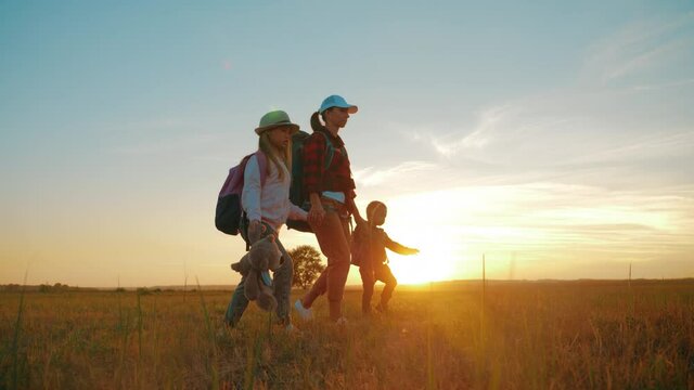 Mother and two children walking in the meadow at the sunset time. Silhouette happy beautiful family during the travelling. Concept of friendly family and travel.