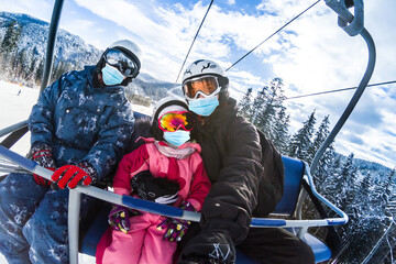 family wearing a medical mask during COVID-19 coronavirus on a snowy mountain at a ski resort