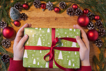 Fototapeta na wymiar Hands holding christmas gift with red ornaments around it