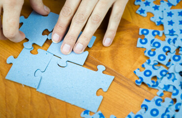 Close-up of a young girl hand collecting jigsaw puzzles on a wooden surface - 393797780