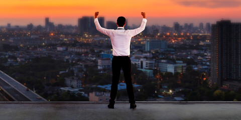 Businessman standing on roof and looking at Cityscape skyline at sunset