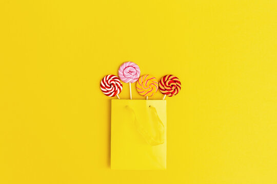 Four sweets round candy lollipop with stripes pattern on stick in yellow paper bag. Trendly minimal style image for greeting card or holiday concept. Flat lay.