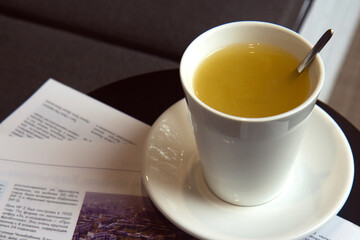 White ceramic cup with hot ginger tea on a table in a cafe. Warming drink. The cup is on the morning newspapers. Morning routine