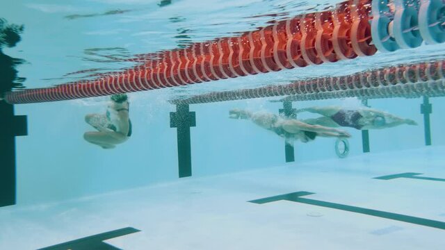Underwater video of swimmers training breaststroke in the indoor swimming pool. They do open turn and swim another lap. 