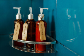 Shampoo, conditiones and shower gel dispensers in brown bottles on te shelf in blue bathroom shower