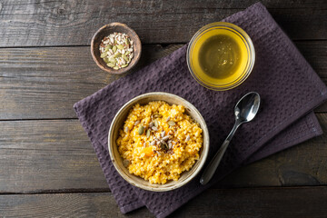 Millet porridge with pumpkin, honey and pumpkin seeds on a dark background. Rustic table with healthy breakfast.