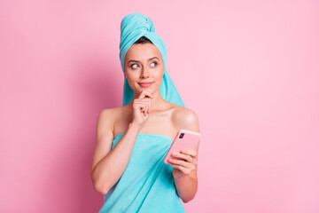 Portrait of nice cute young lady hold telephone look empty space finger chin wear teal bath clothes isolated on pastel pink color background