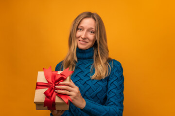 Charming young woman open a gift with red ribbon. Studio shot, yellow background. New Year, Birthday, Holiday concept
