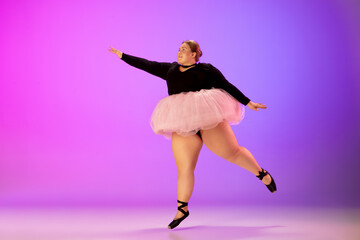 Confidence. Beautiful caucasian plus size model practicing ballet dance on gradient purple-pink studio background in neon light. Concept of motivation, inclusion, dreams and achievements.