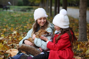 Two girls holding fox in her arms in autumn park