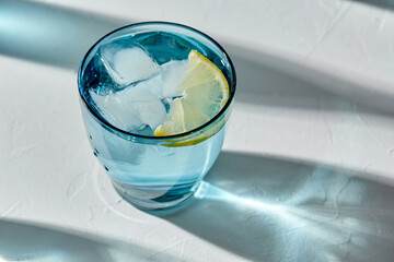 drink, detox and diet concept - blue glass of water with lemon and ice on white background