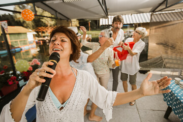 Senior people celebrating birthday in the cottage on the river singing karaoke.