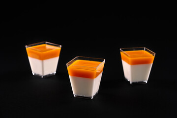 Small square glasses with panna cotta isolated on black.