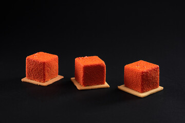 Three orange square cakes with matte surface in row.